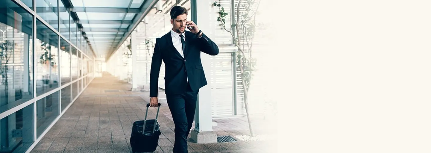 Professional businessman with suitcase talking on phone in modern corridor - representing immigration and business travel services